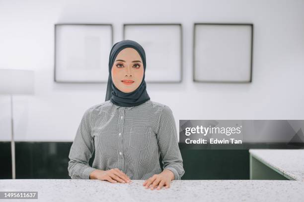 asian muslim female office receptionist concierge looking at camera smiling front view standing in front of counter - hotel opening party stock pictures, royalty-free photos & images