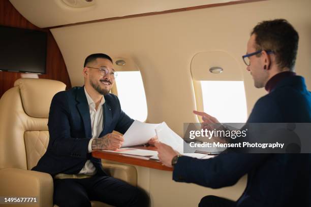confident young businessman ceo discussing a job with his manager talking about work in private airplane jet - billionaire stock pictures, royalty-free photos & images