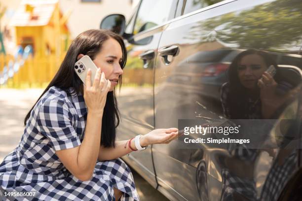 a woman who found her car dented by a scratch knees next to her car and calls to find out what can she do about it. - abollado fotografías e imágenes de stock