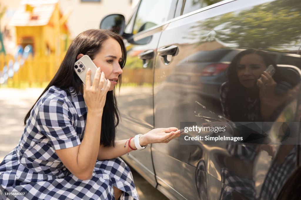 A woman who found her car dented by a scratch knees next to her car and calls to find out what can she do about it.
