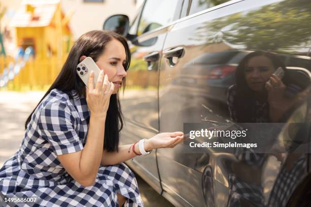 a woman who found her car dented by a scratch knees next to her car and calls to find out what can she do about it. - auto-ongeluk stockfoto's en -beelden
