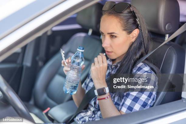 beautiful woman sits in a car during summertime, swallowing a pill and drinking water from a plastic bottle. - schmerzmittel stock-fotos und bilder