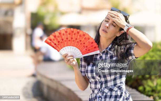 woman uses hand fan to cool down when summer heat wave hits the city. - ondata di calore foto e immagini stock