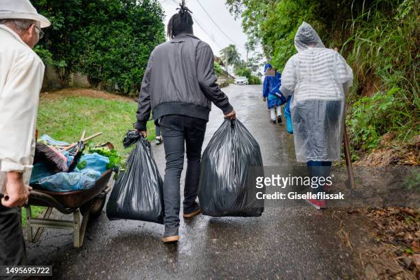 des personnes portant des sacs d’un jardin remontent une allée sous la pluie - sac poubelle photos et images de collection