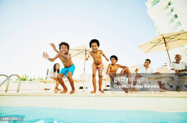 wide shot young brothers jumping into swimming pool at tropical resort - bermuda shorts stock pictures, royalty-free photos & images