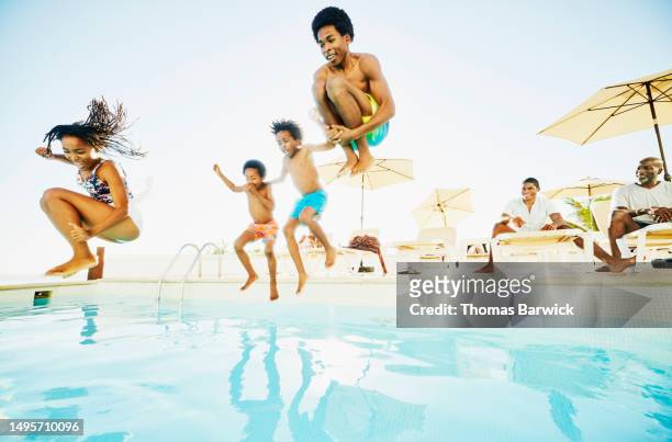 Wide shot siblings jumping into swimming pool at tropical resort