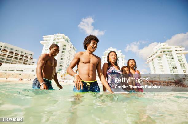 wide shot of smiling siblings playing in ocean during family vacation - all inclusive holiday stock pictures, royalty-free photos & images