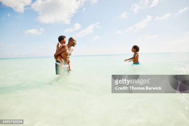 wide son father carrying young son on back while playing in ocean - quintana roo stock-fotos und bilder