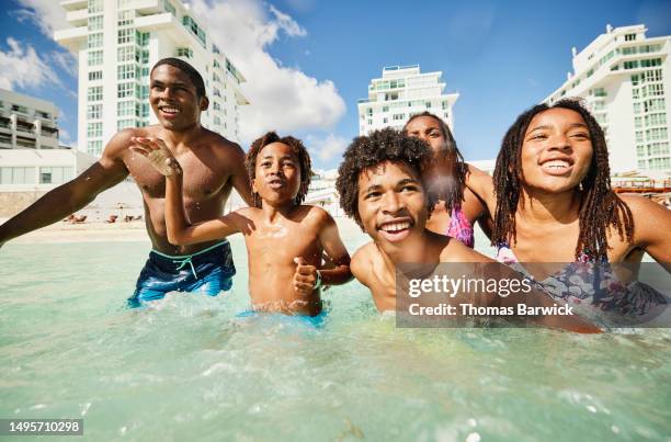 medium shot family playing in waves in  ocean during family vacation - medium group of people fotografías e imágenes de stock