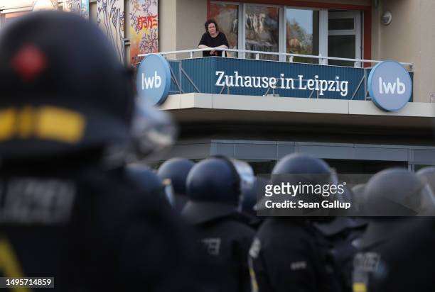Woman on an apartment balcony looks out at police clad in riot gear as an advertising banner reads: "At home in Leipzig" during the leftist "Day X"...