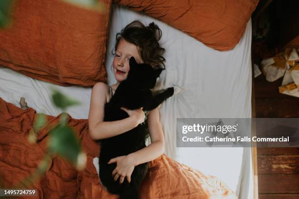 a little girl lies in bed, hugging her cat. - kids kindness stock pictures, royalty-free photos & images