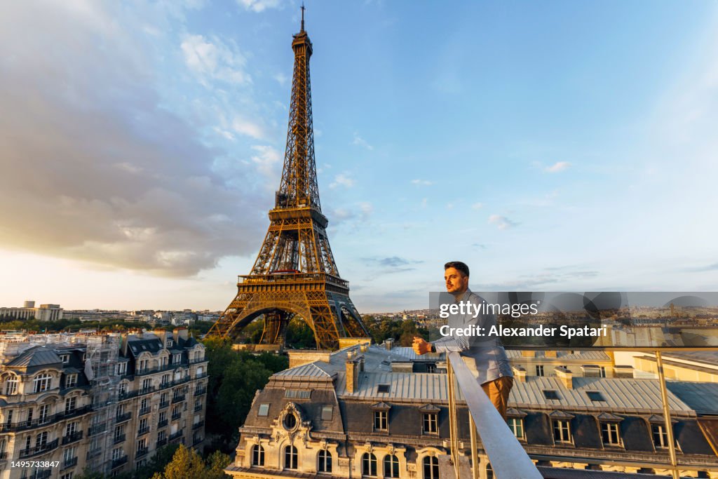 Young man looking at the sunset from the balcony with Eiffel Tower in the background, Paris, France