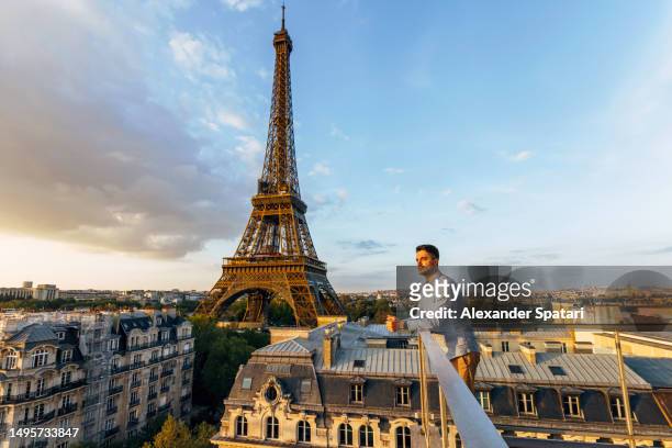 young man looking at the sunset from the balcony with eiffel tower in the background, paris, france - paris france hotel stock pictures, royalty-free photos & images