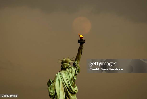 An almost full Strawberry Moon rises through clouds behind the Statue of Liberty following a thunderstorm in New York City on June 2 as seen from...