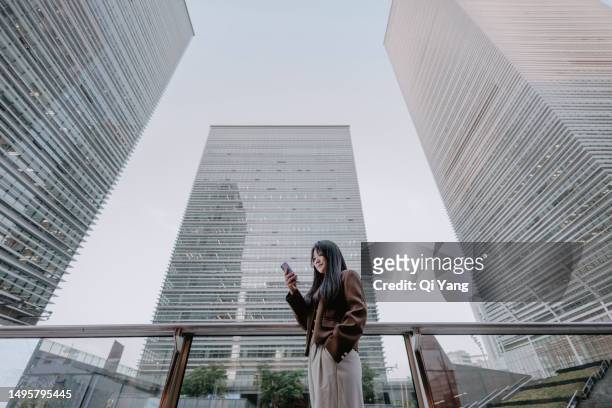 asian businesswoman using smartphone under financial building in shanghai, china - businesswoman under stock-fotos und bilder