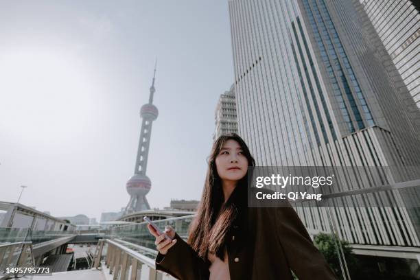 business woman standing in front of the landmark oriental pearl tv tower in shanghai, china - pudong stock-fotos und bilder