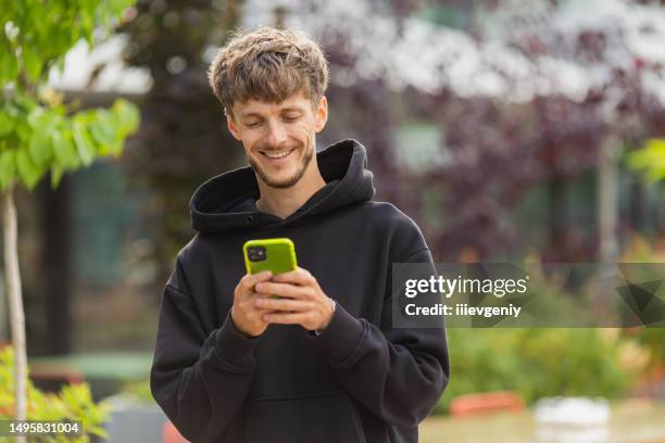 happy young man with smartphone outdoors. blurred summer background. mobile phone - zoom imagens e fotografias de stock