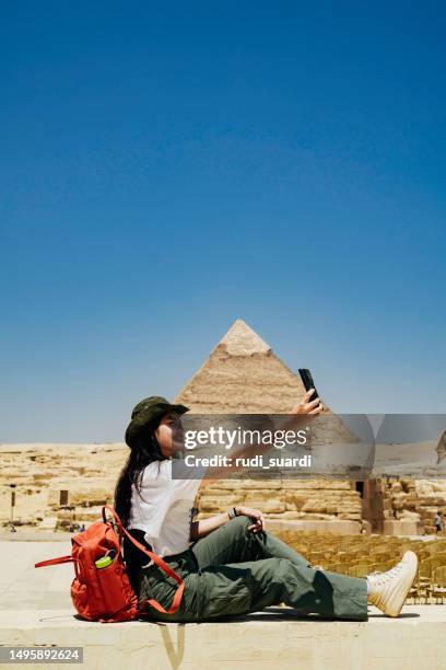 ägypten, kairo, asiatische touristin, die auf felsen sitzt, mit der großen pyramide von gizeh im hintergrund - pyramiden von gizeh stock-fotos und bilder