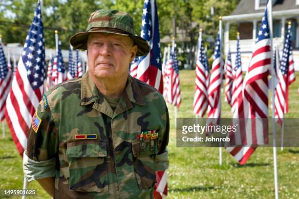 un vétéran de la guerre du vietnam parmi les drapeaux américains regarde ailleurs - us military emblems photos et images de collection