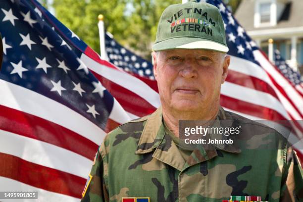 vétéran de la guerre du vietnam parmi les drapeaux américains regardant la caméra - us military emblems photos et images de collection