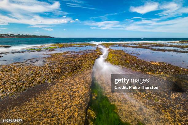 meereslandschaft mit wasserwellen, die an einem perfekten, klaren sonnentag über felsen am strand fließen - gezeiten stock-fotos und bilder