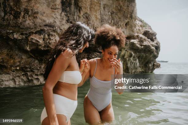 two woman on a beach holiday experience joy as they paddle in the ocean - baño-de-pies fotografías e imágenes de stock