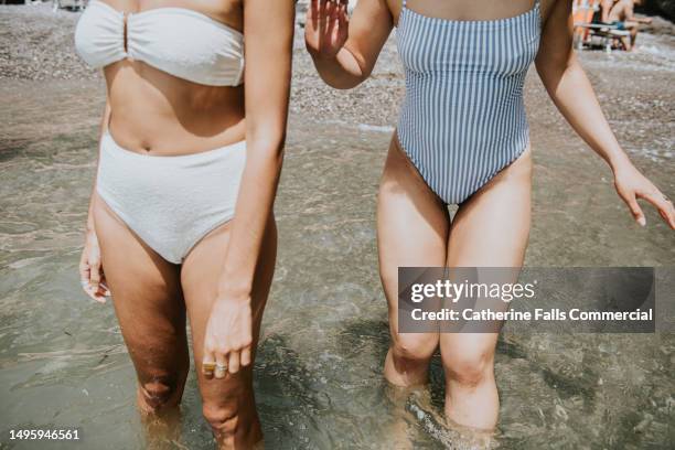 close-up of the legs of two woman wearing swimwear, paddling in the ocean - dijbeen menselijk been stockfoto's en -beelden