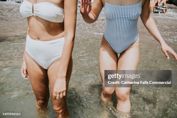 close-up of the legs of two woman wearing swimwear, paddling in the ocean - swimwear store stock pictures, royalty-free photos & images