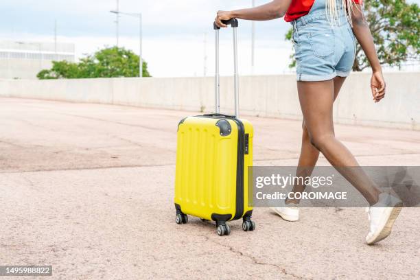 young woman walking with a travel suitcase on wheels while going to spend a few days on vacation. - yellow suitcase stock pictures, royalty-free photos & images