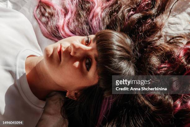 close-up portrait of a brown-eyed young woman under the setting sun. long shadows. charming brunette girl with beautiful long curly highlighted hair and pink strands. - sun on face stock-fotos und bilder