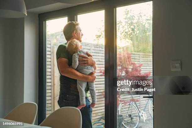 mature father holding his sleeping baby daughter whilst he looks out over their garden in the lovely late afternoon sun - father holding sleeping baby stockfoto's en -beelden