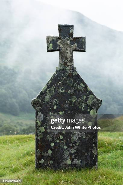 tombstone covered with moss and lichen. misty mountain in the background. scotland. - grabstein stock-fotos und bilder