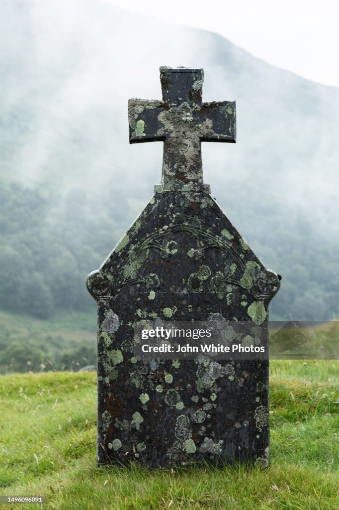 Tombstone covered with moss and lichen. Misty mountain in the background. Scotland.
