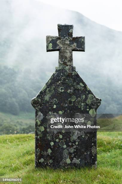 tombstone covered with moss and lichen. misty mountain in the background. scotland. - grafsteen stockfoto's en -beelden