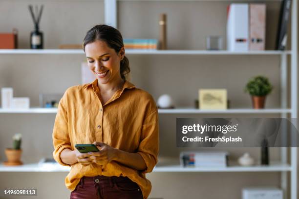 eine glückliche schöne blonde geschäftsfrau, die ihr mobiltelefon benutzt, während sie im büro arbeitet - businesswoman talking smartphone stock-fotos und bilder