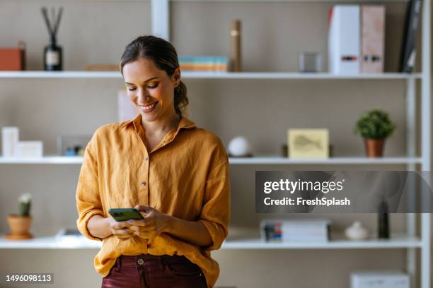 una bella donna d'affari bionda felice che usa il suo telefono cellulare mentre lavora in ufficio - women 35 foto e immagini stock