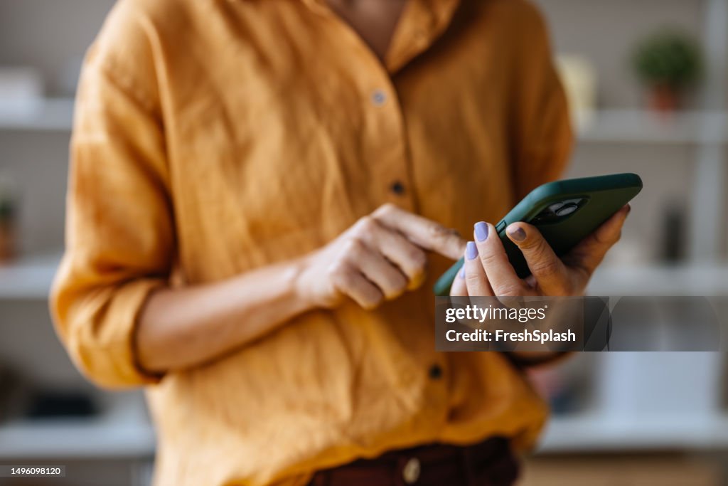 An Unrecognizable Businesswoman Using Her Mobile Phone While Working In The Office