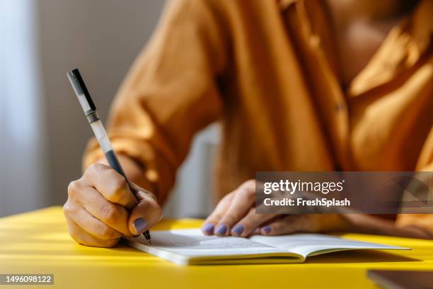 una mujer de negocios irreconocible tomando algunas notas en su cuaderno mientras trabaja en la oficina - writing instrument fotografías e imágenes de stock