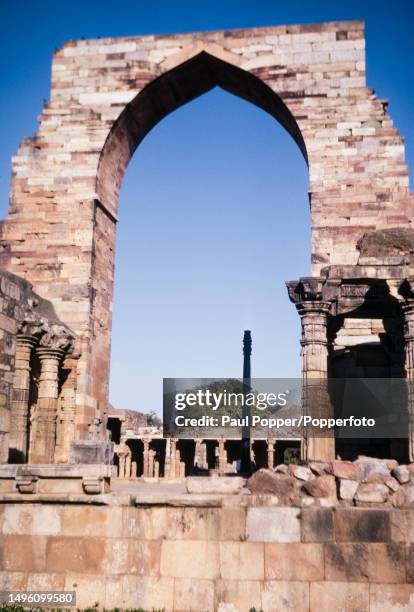 An arch from the ruined Quwwat-ul-Islam mosque stands in front of the Iron Pillar within the Qutb Minar complex of monuments in the Mehrauli district...