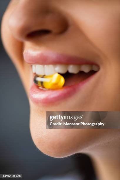 young woman holding pill omega-3 fish oil in mouth between teeth, close-up - fish oil stock pictures, royalty-free photos & images