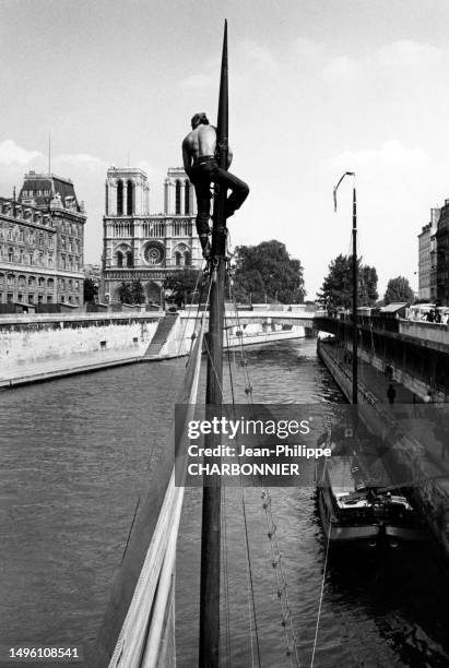 Marin escaladant le mât d'un bateau à voile sur la Seine à Paris, circa 1960.