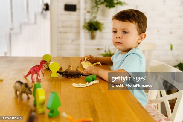 garotinho curioso brincando com brinquedo de dinossauro na mesa - dinosaur toy i - fotografias e filmes do acervo