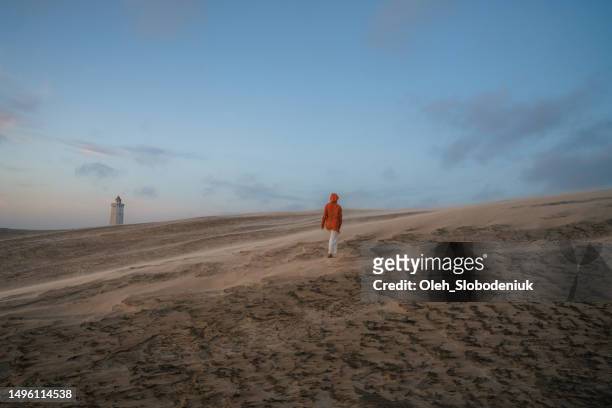 woman walking on the background of rubjerg knude lighthouse during sandstorm - north sea denmark stock pictures, royalty-free photos & images