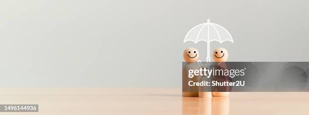 Happy family under the umbrella on raining wooden figurine model on table top background. People lifestyles and Relationships in love concept.