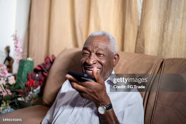 senior man sending audio message on the phone in the living room at home - direct stock pictures, royalty-free photos & images