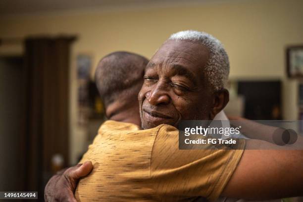 bonding moment of father and son embracing and giving emotional support at home - senior embracing stock pictures, royalty-free photos & images