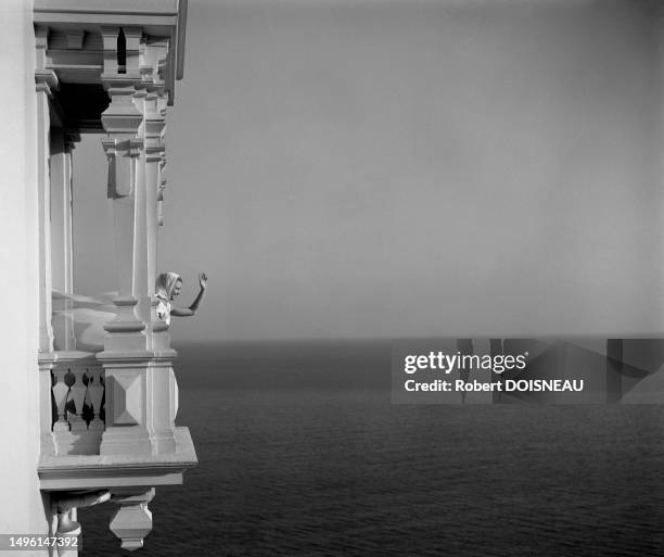 Une femme salue de la main depuis un balcon donnant sur la Mer Méditerranée à l'été 1961 sur la Côte d'Azur.