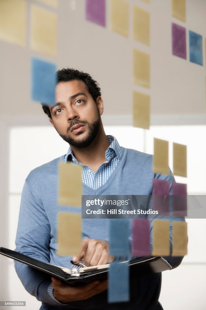 Mixed race businessman looking at sticky notes in office