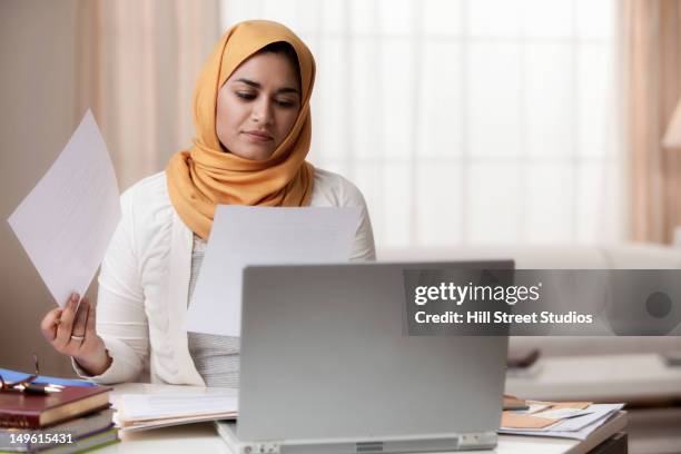 mixed race woman in hijab looking at paperwork - headscarf home stockfoto's en -beelden