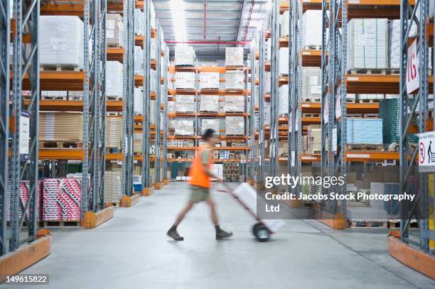 worker pushing hand truck in warehouse - lagerhalle stock-fotos und bilder